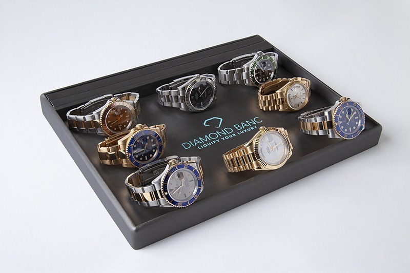 A display of 8 luxury watches, featuring various styles and colors, arranged in a sleek tray with "Diamond Banc" logo prominently shown.