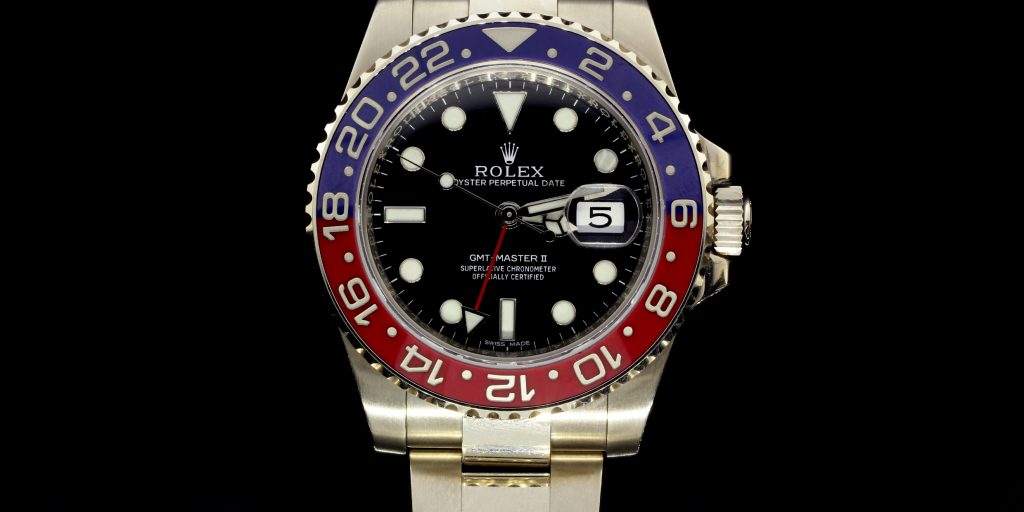 Close-up of a Rolex GMT-Master II watch with a black dial, red and blue bezel, and stainless steel bracelet, showcasing luxury and craftsmanship.