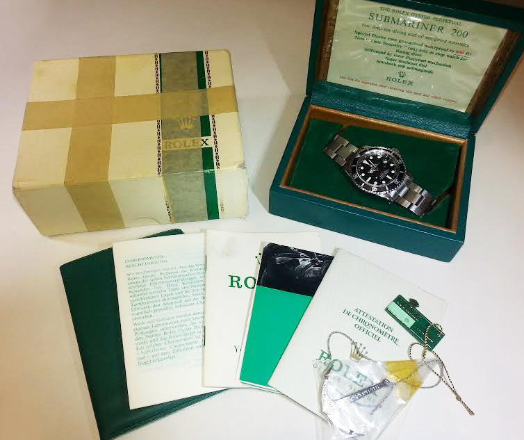 A Rolex Submariner watch in a green box, accompanied by manuals, certification, and the original packaging, showcasing luxury timekeeping.