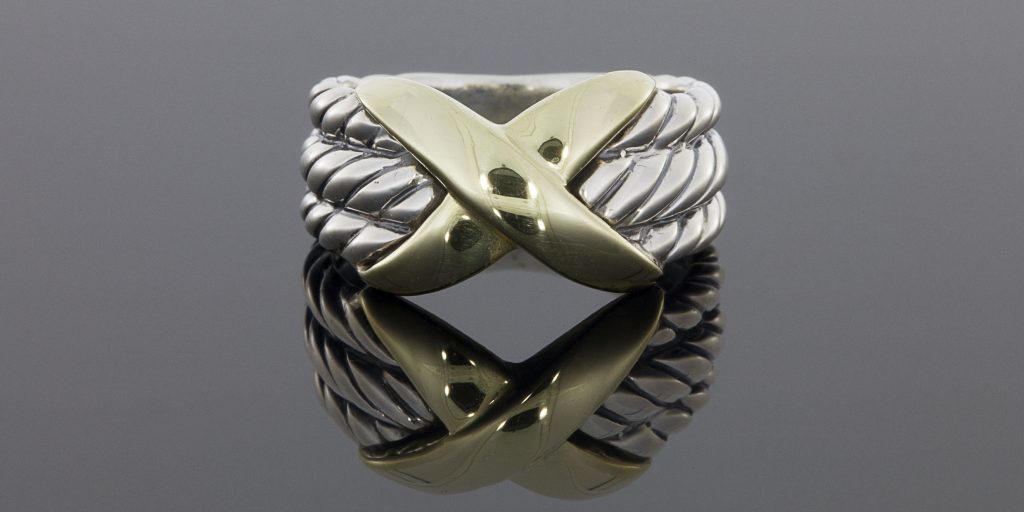 This beautiful ring is from the Crossover Collection and features this signature cable design. It features 3 sterling silver, cable designed rows with a yellow gold "X" in the center. The ring measures 11mm wide at the top, tapering to 5mm at the base. It is currently a finger size 6.25 and is sizable upon request. This ring retails for $495 but we are selling it for $350!
