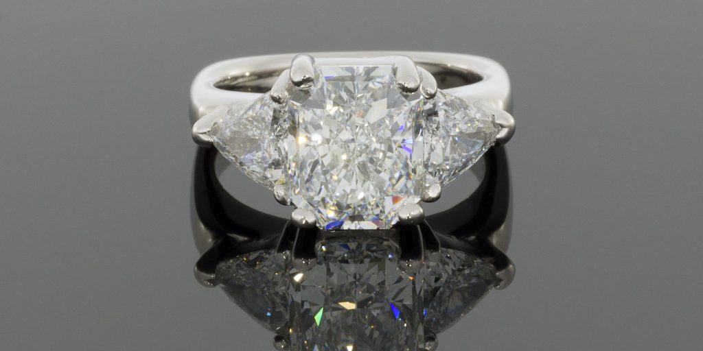 Elegant three-stone diamond ring featuring a central radiant-cut diamond flanked by two triangular-cut diamonds, set in polished white gold.