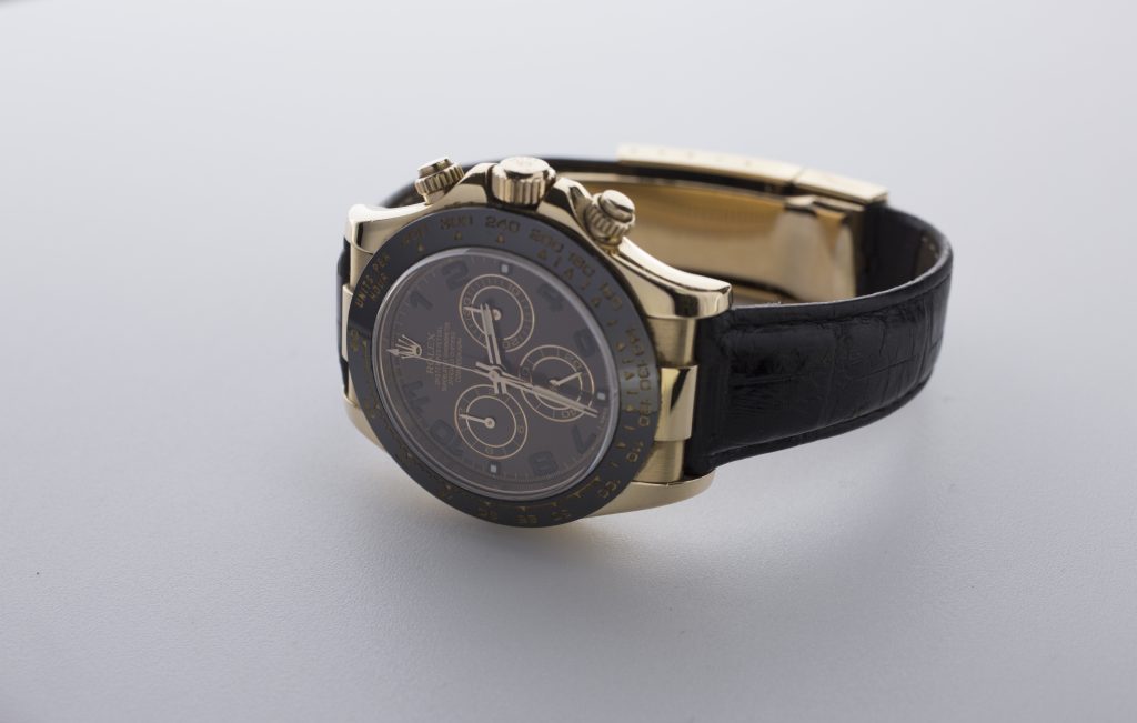 A Rolex Cosmograph Daytona watch with a black leather strap, featuring a dark dial and multiple dials for time and stopwatch functions.