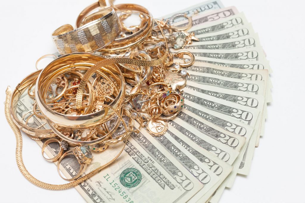 A pile of assorted gold jewelry interspersed with stacks of twenty-dollar bills on a white background.