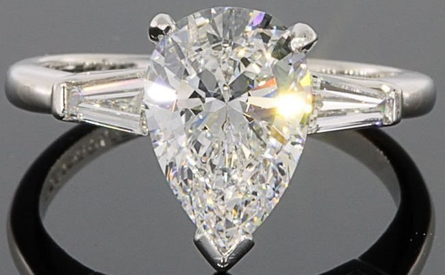 A stunning pear-shaped diamond engagement ring with side baguette stones, set in a sleek white gold band against a dark background.
