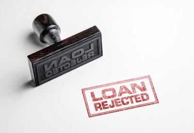 A rubber stamp labeled "LOAN REJECTED" sits next to a stamped red "LOAN REJECTED" mark on a white surface