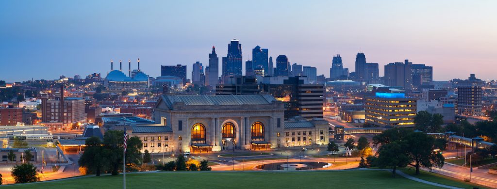 Panoramic view of Kansas City's skyline at twilight, featuring the iconic Union Station and illuminated buildings in the background.