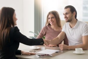 A business meeting at a table where one person shakes hands with another, with documents and cups on the table.