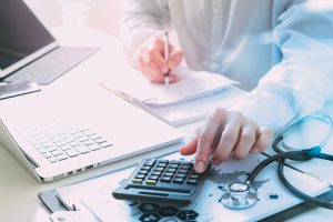 A doctor in front of a laptop while using calculator to calculate medical expenses of patients
