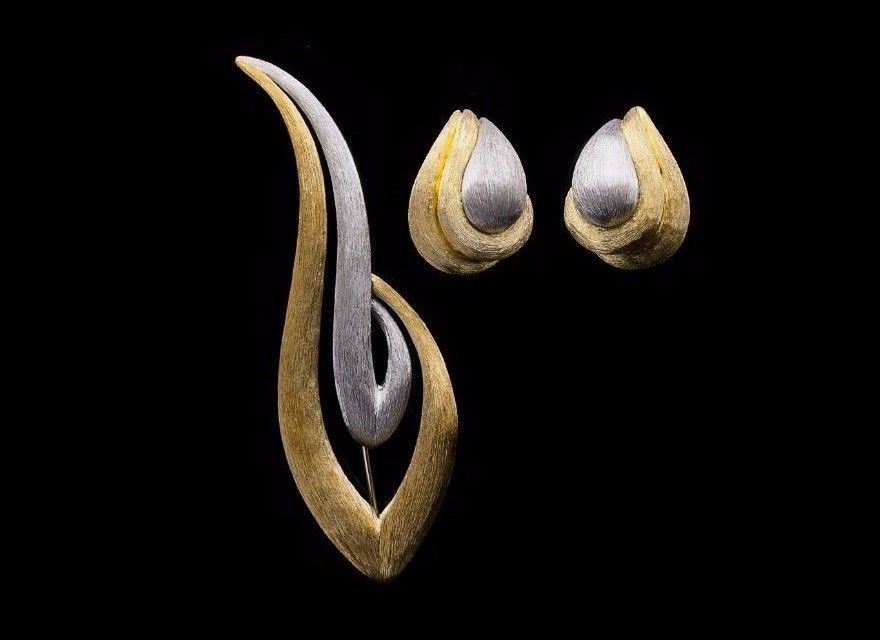 Elegant gold and silver earrings and a matching decorative pin, featuring flowing, curved designs against a black background.