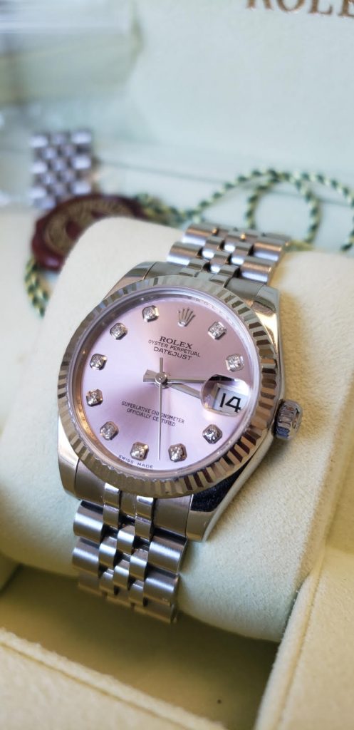 A luxurious silver Rolex datejust watch with pink dial displayed on a soft cream cushion, showcasing its elegant design and classic bracelet.