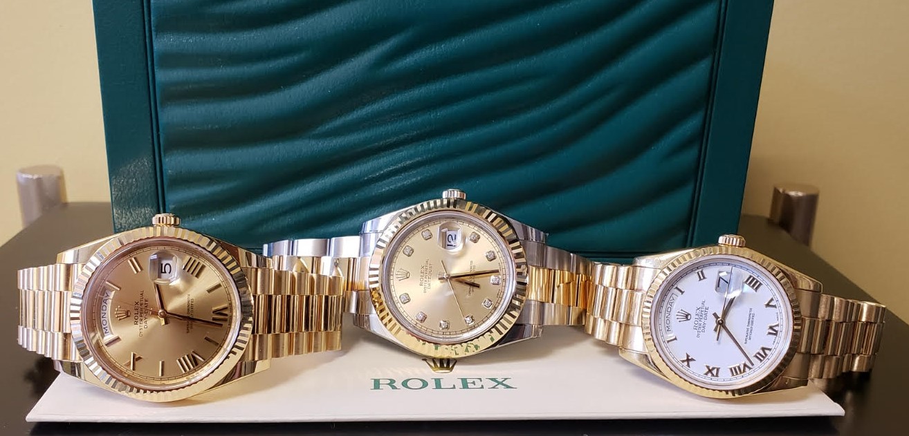 Three luxurious Rolex watches displayed on a white watch box, featuring gold and silver tones with different dials and Roman numerals.
