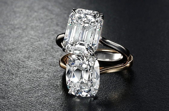 Two different cut diamond engagement rings on a black surface.