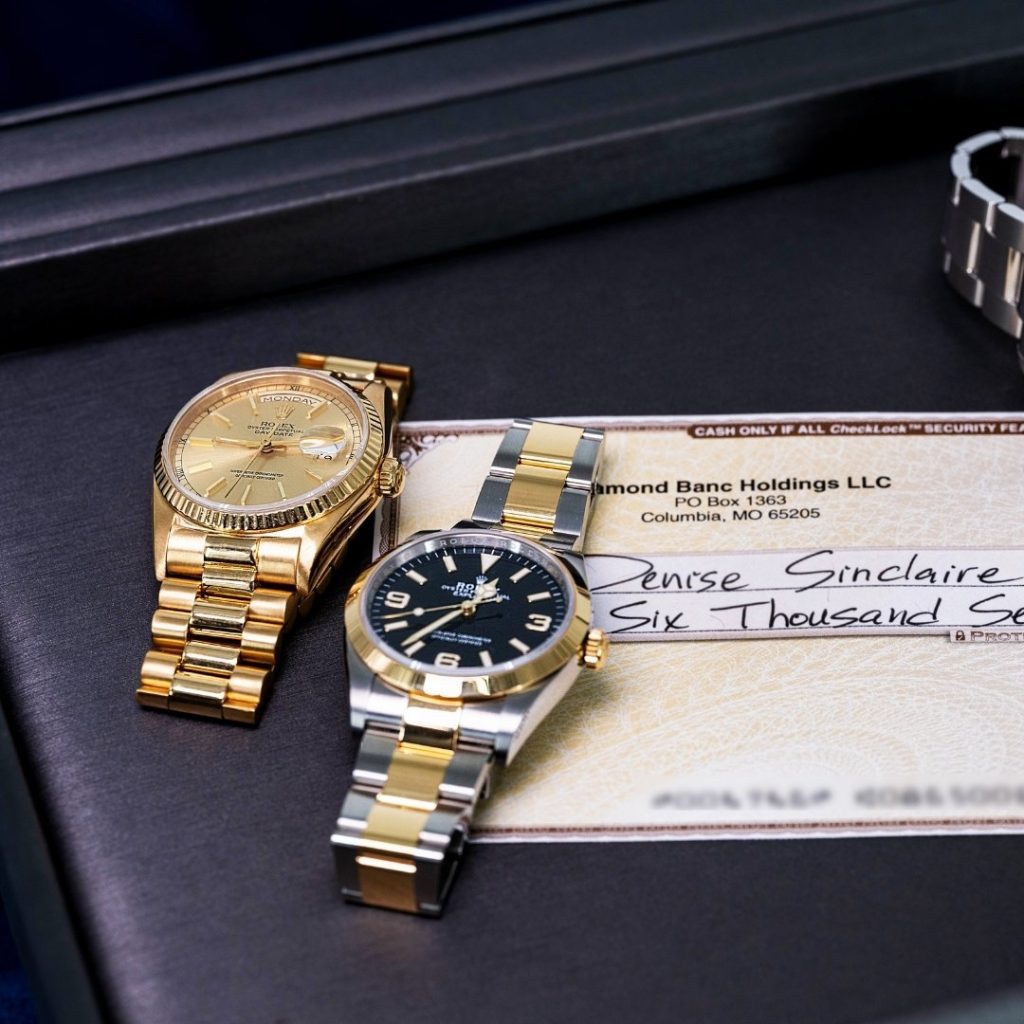 A gold and silver luxury watch pair beside a check made out to Denise Sinclair for six thousand dollars.