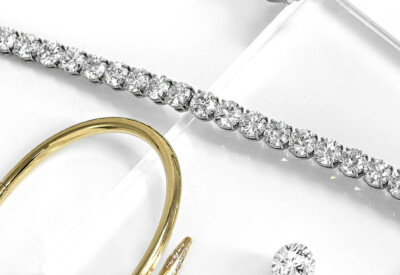 Image of gold nail bracelet with diamonds, a white gold diamond tennis bracelet, a loose round diamond, and an emerald diamond engagement ring - Diamond Banc | The Nation's Premier Diamond Buyer