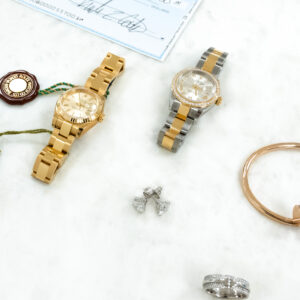 Image of two lady's rolex watches, a tiffany ring, cartier bracelet, diamond earrings and a paper check