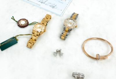 Image of two lady's rolex watches, a tiffany ring, cartier bracelet, diamond earrings and a paper check