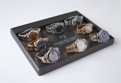 A display of 8 luxury watches, featuring various styles and colors, arranged in a sleek tray with "Diamond Banc" logo prominently shown.