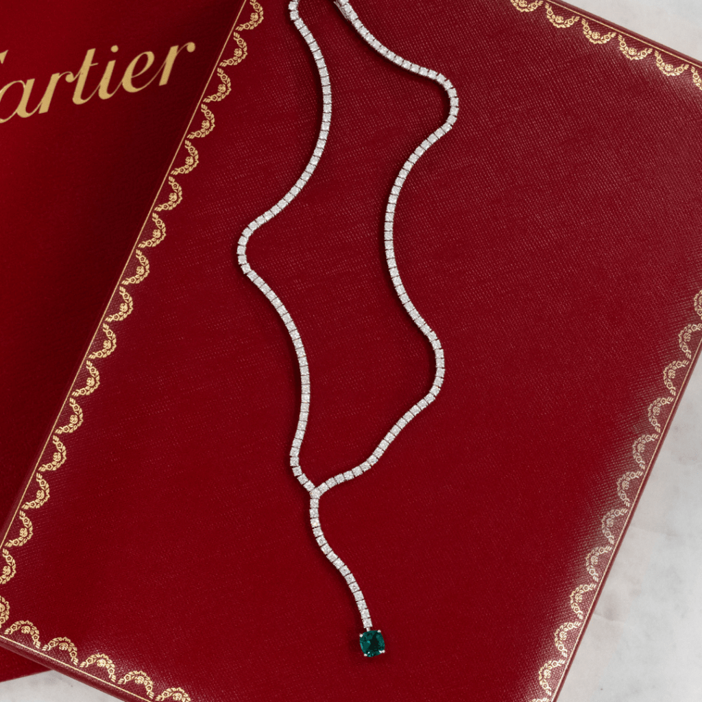 Featuring a Cartier diamond necklace with a vibrant green emerald pendant on a Cartier box, positioned above a Cartier certificate folder, Diamond Banc is the premier destination for clients interested in selling their luxury jewelry to a reputable jewelry buyer in Sarasota.