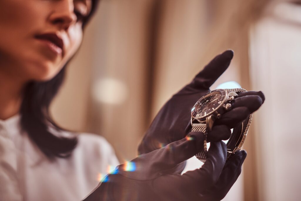A trusted Rolex buyer wearing black gloves holds and examines a wristwatch, with their face partially visible in the background.