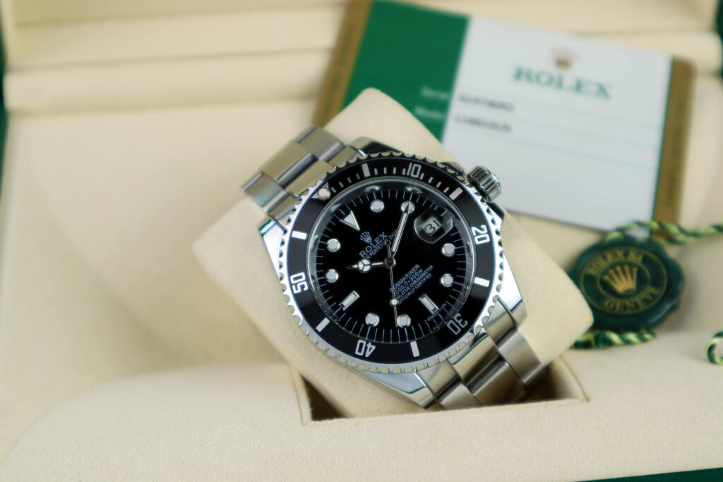 A stainless steel Rolex Submariner watch with a black dial and bezel, displayed in its box alongside the iconic Rolex warranty card and green tag.