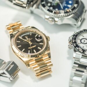 A close-up of three luxury wristwatches with metal bands, including gold and silver finishes, displayed on a white surface.