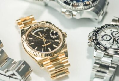 A close-up of three luxury wristwatches with metal bands, including gold and silver finishes, displayed on a white surface.