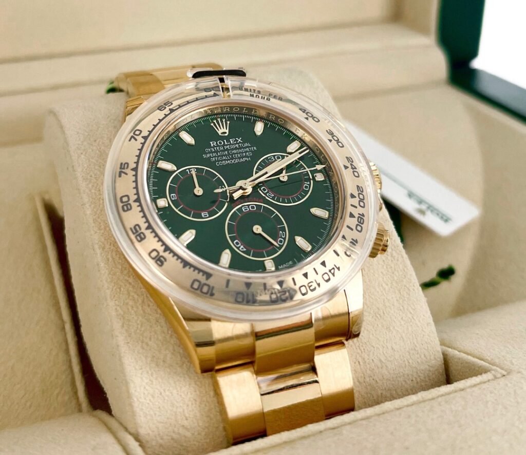 A gold Rolex Daytona watch with a green dial is displayed in an open Rolex box.