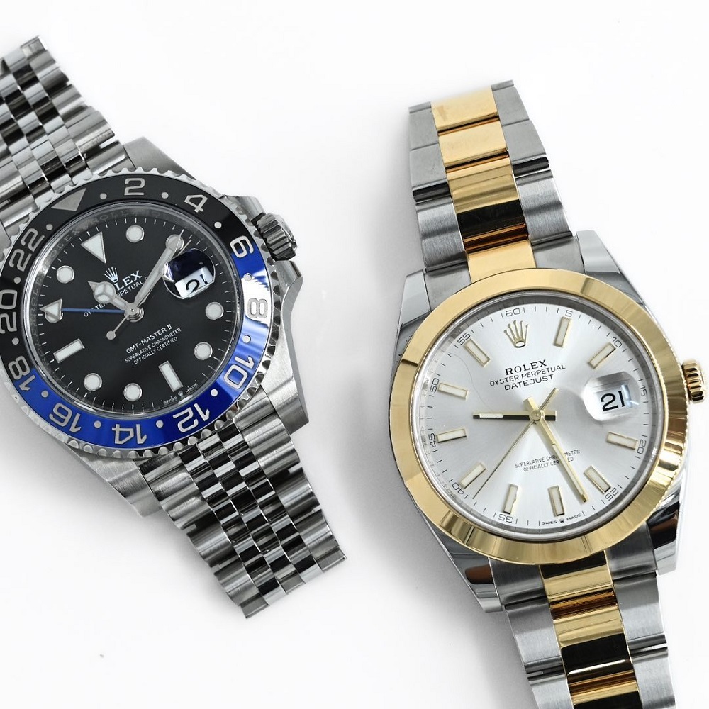 	
Two Rolex wristwatches displayed side by side; one Rolex boasts a black and blue bezel with a dark dial, while the other features a white dial and a gold and silver two-tone bracelet.
